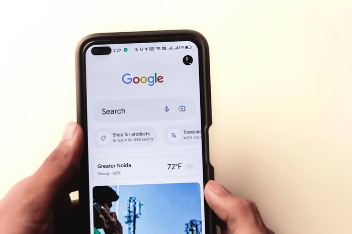 A close-up of a hand holding a smartphone with Google search displayed on the screen.