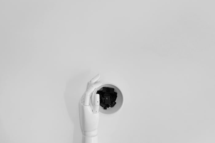 A robotic hand grasping black keyboard keys in a minimalist setting.
