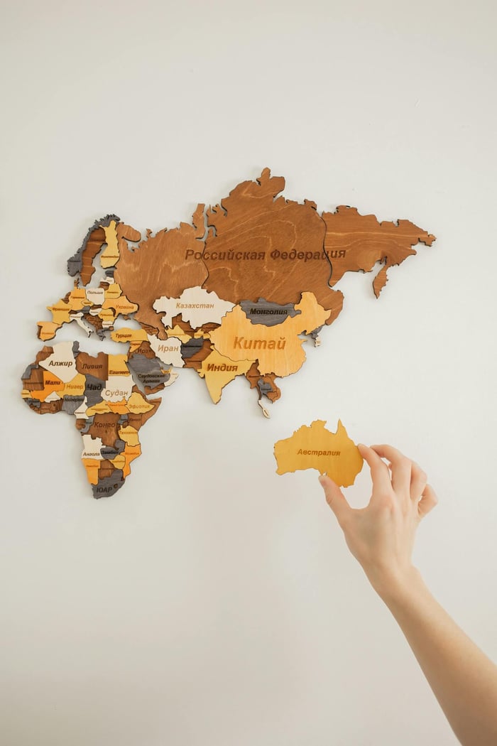 Hand arranging a wooden map decoration on a white wall.